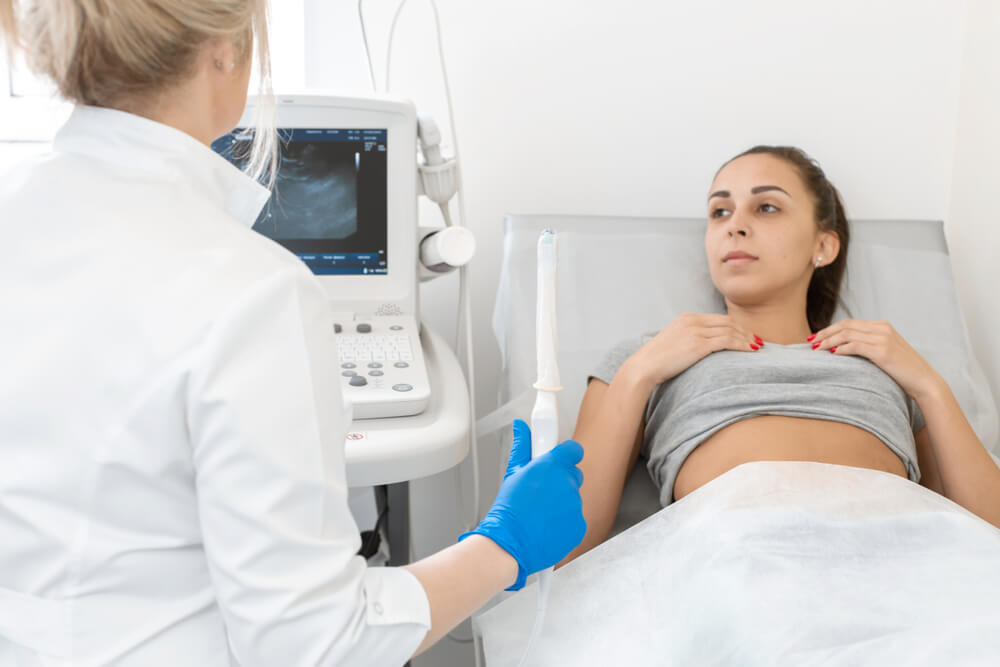 A gynecologist sets up an ultrasound machine to diagnose a patient who is lying on a couch. A transvaginal ultrasound scanner of the internal organs of the pelvis. Female health concept.
