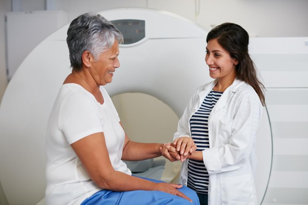 Doctor, ct scan and woman holding hands of patient in hospital before scanning in machine. Mri, comfort and happy medical professional with senior female person before radiology test for healthcare.