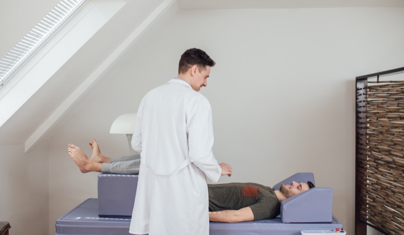 Young Caucasian medical technician operating the bone densitometer while his patient is lying on the bed.