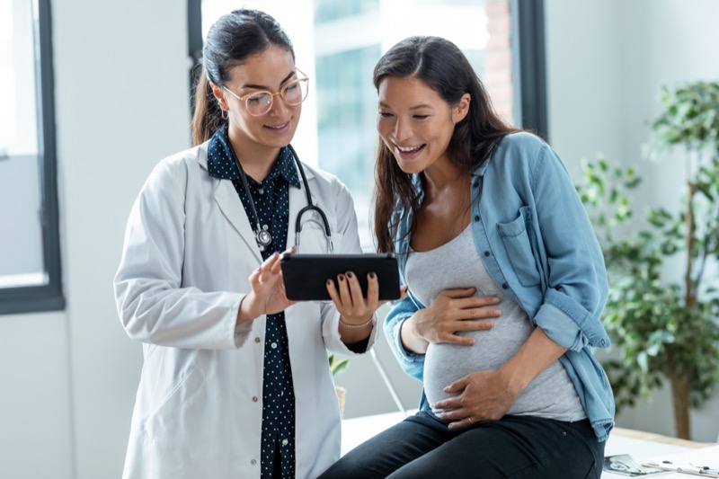 Shot of female gynecologist doctor showing to pregnant woman ultrasound scan baby with digital tablet in medical consultation.