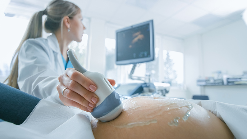 In the Hospital, Close-up Shot of the Doctor does Ultrasound / Sonogram Procedure to a Pregnant Woman. Obstetrician Moving Transducer on the Belly of the Future Mother.