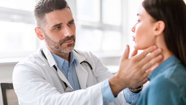 Medicine, healthcare and medical check up concept. Male doctor checking patient's tonsils at hospital. Endocrinologist examining throat of young lady in clinic