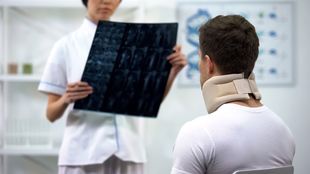 Traumatologist showing neck xray to male in foam cervical collar, bad diagnosis