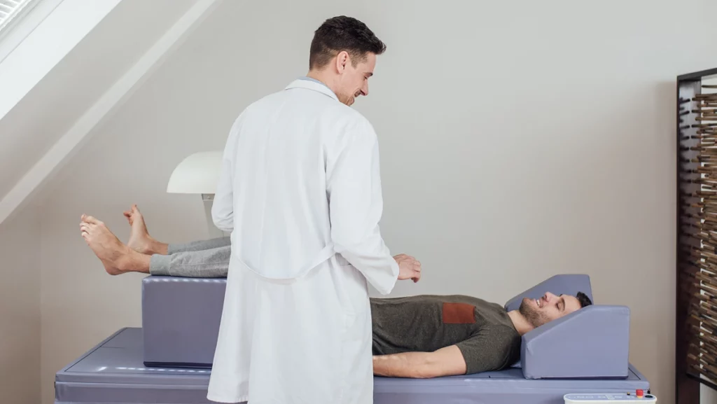 Young Caucasian medical technician operating the bone densitometer while his patient is lying on the bed.